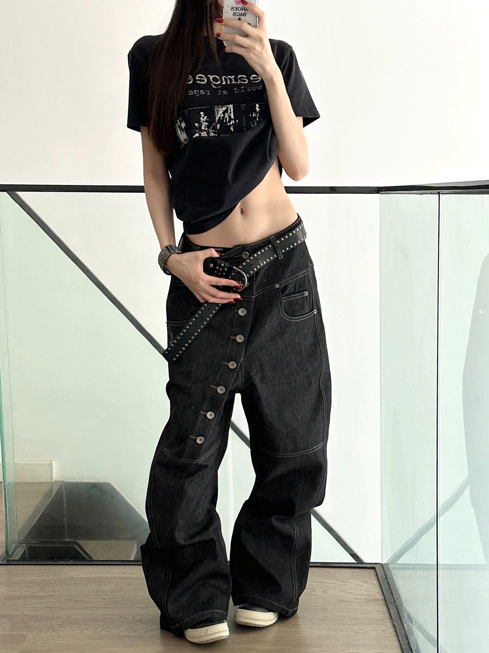 Front view of asymmetric button fly wide-leg denim pants with utility pockets and studded leather belt styling