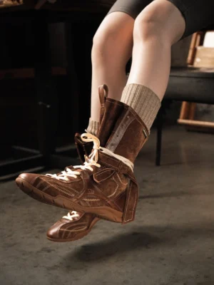Model wearing dark brown lace-up mid-calf utility boots with ribbed socks in an indoor lifestyle setting