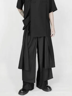 Front view of black avant-garde asymmetric draped wide-leg trousers with layered skirt overlay and relaxed darkwear silhouette