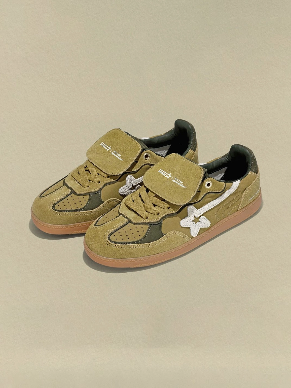 Pair of avocado suede star-panel retro sneakers shown in a front three-quarter view with detachable tongue straps and low-profile silhouette