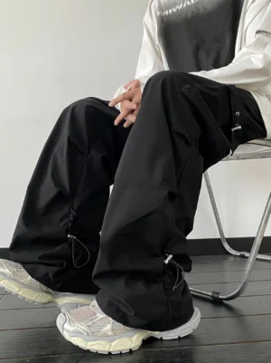 Black baggy cargo pants with adjustable drawstring ankles and utility side pockets styled with chunky sneakers in a low-angle streetwear outfit