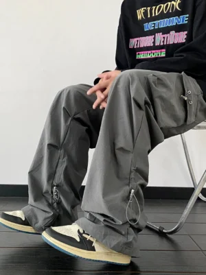 Dark gray baggy drawstring hem cargo pants styled with a black graphic sweatshirt and retro basketball sneakers in a low-angle seated streetwear look