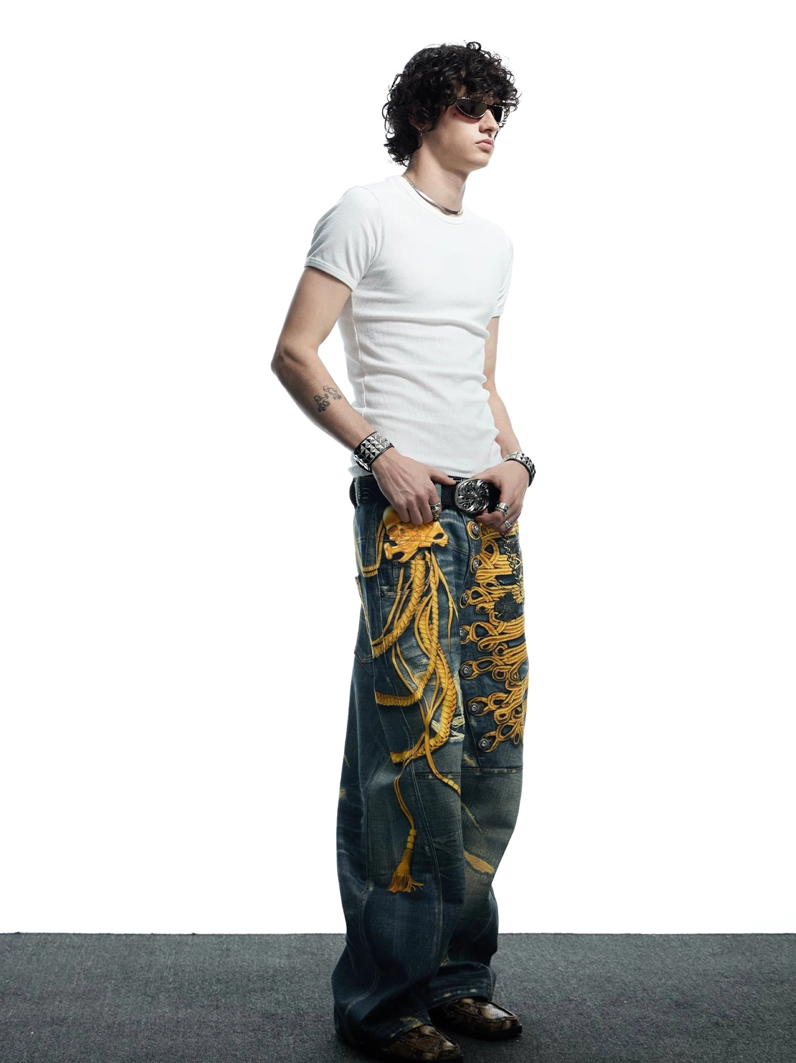 Side profile of men's distressed wide-leg jeans with baroque military gold embroidery and faded dark denim texture