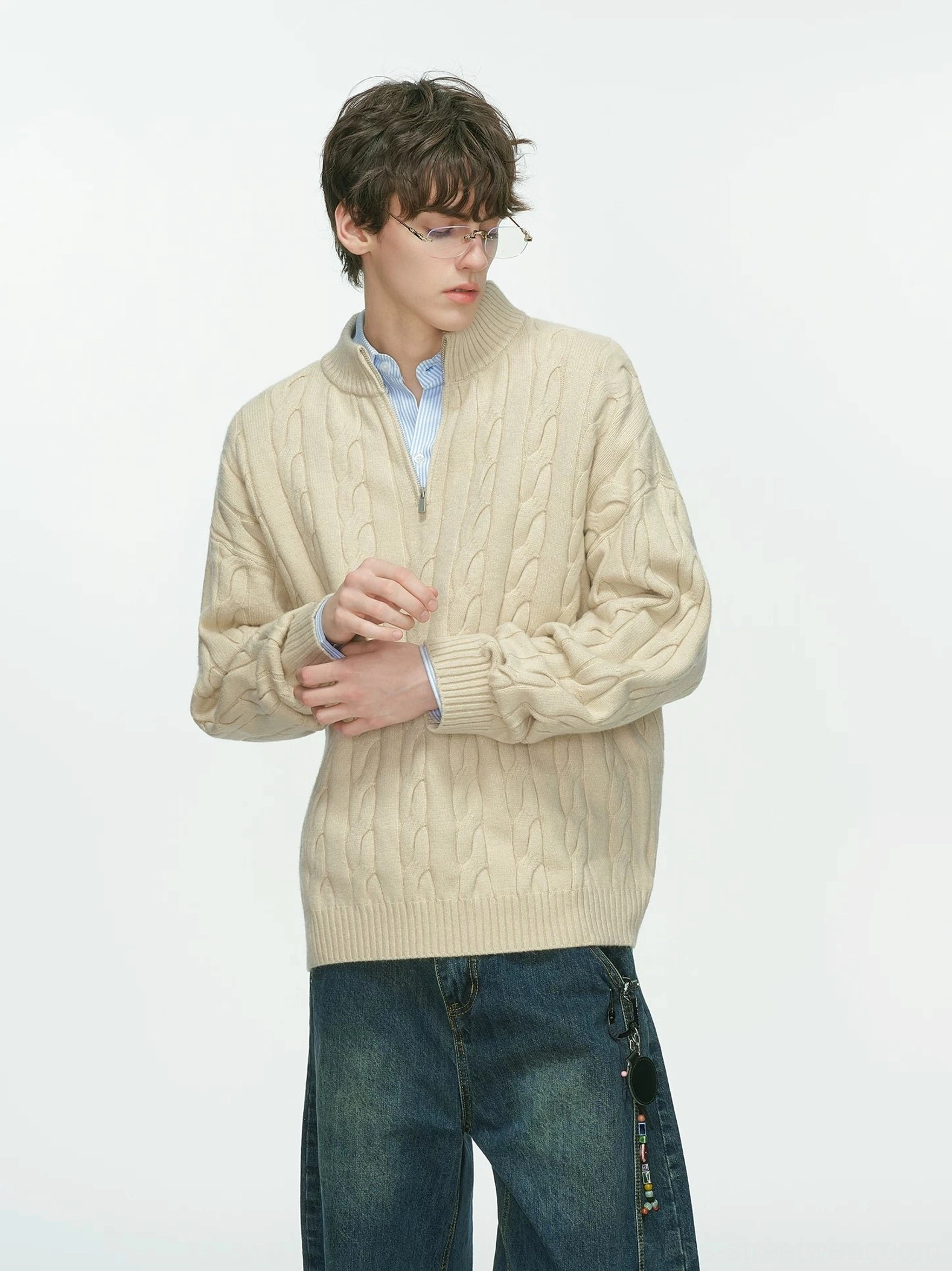 Beige cable-knit half-zip sweater with stand collar and loose sleeves styled with a blue shirt and dark wide-leg jeans