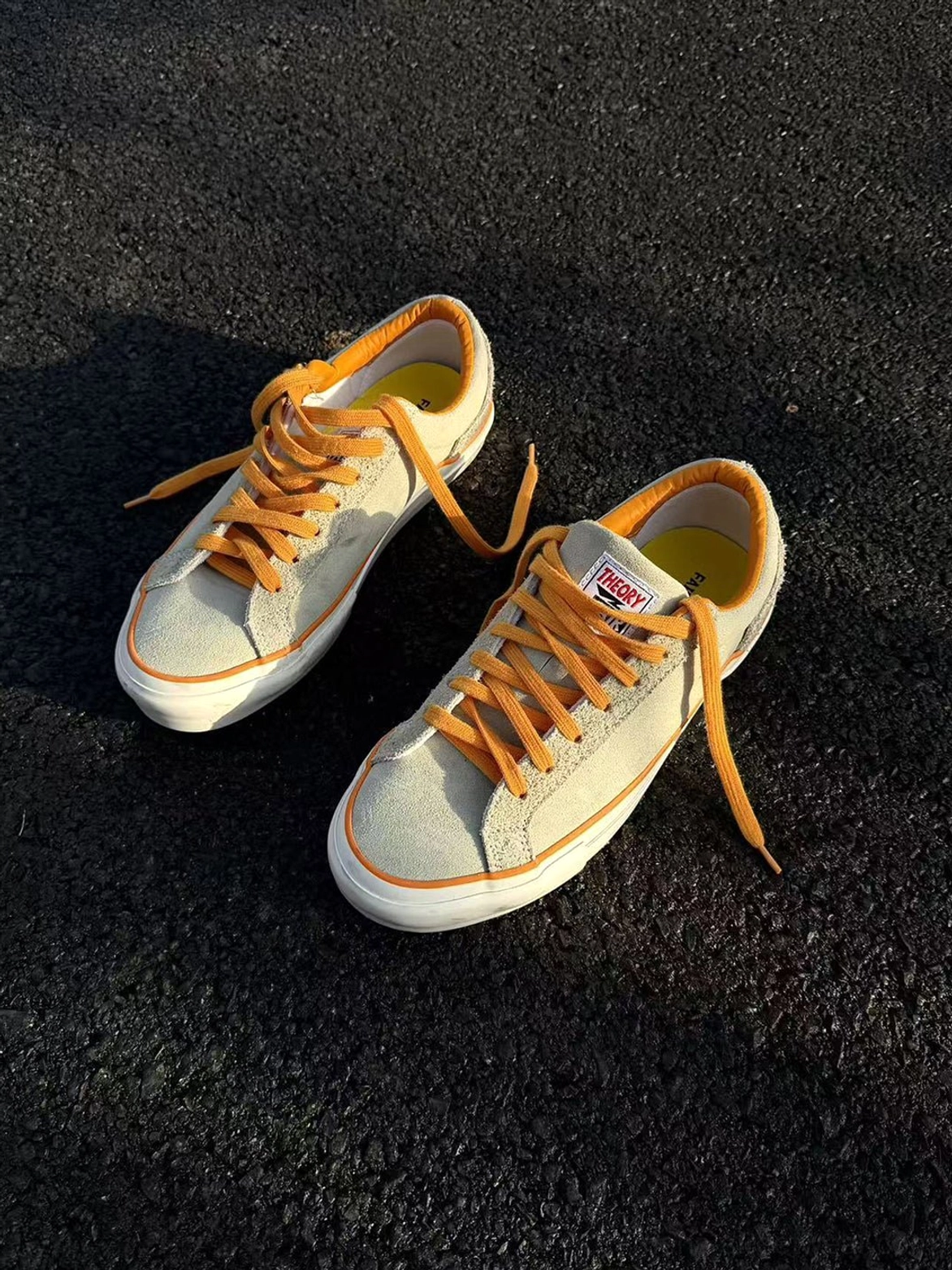 Pair of beige colorblock suede skate shoes displayed on asphalt with orange laces, tongue details, and clean rubber outsoles