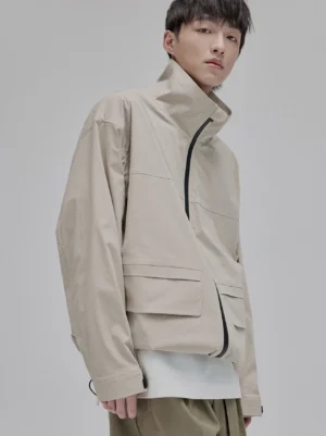 Beige high-neck structural windbreaker jacket in a relaxed streetwear fit with front zipper and flap cargo pockets