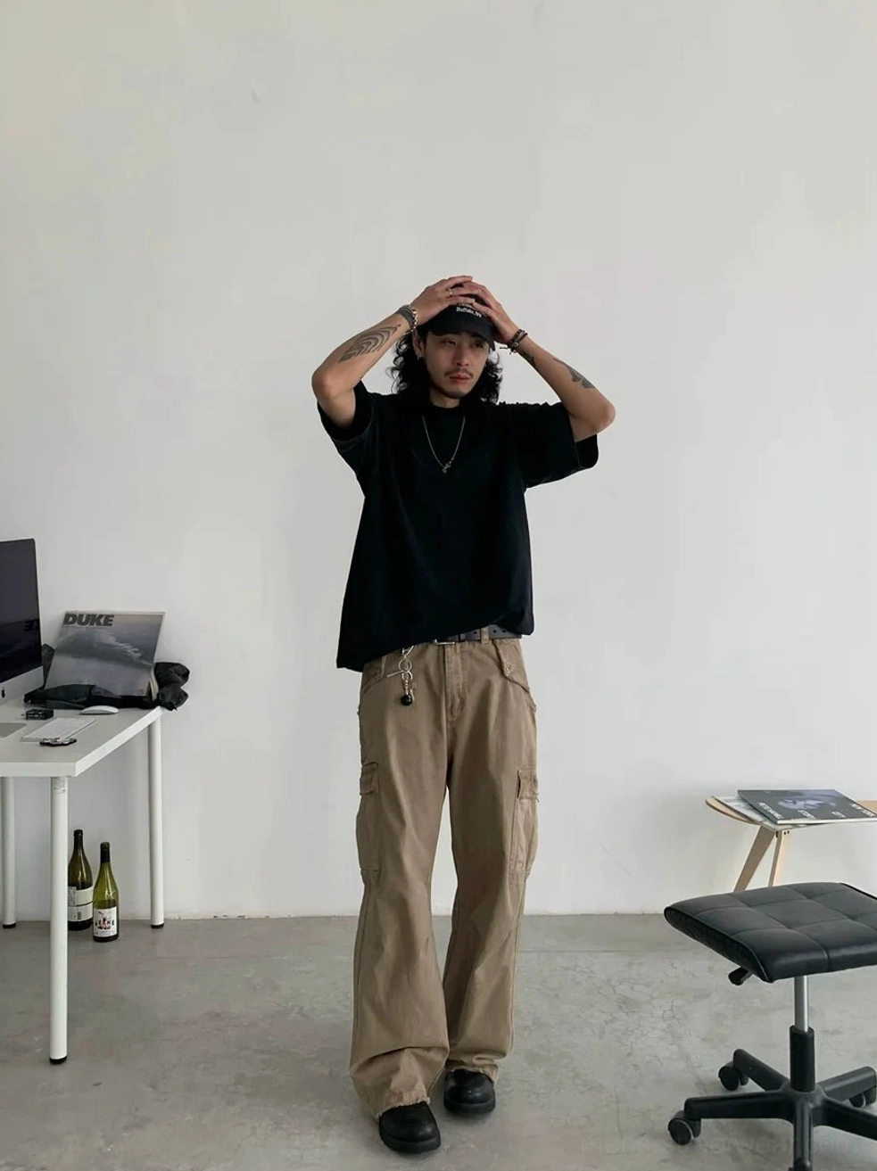 Front view of loose beige cargo pants with multiple utility pockets styled with a backwards baseball cap for a casual Korean streetwear outfit