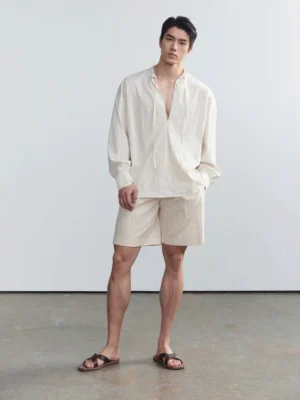 Beige men's tie-neck relaxed long sleeve shirt in Korean minimalist style shown in a full-body studio outfit with matching shorts