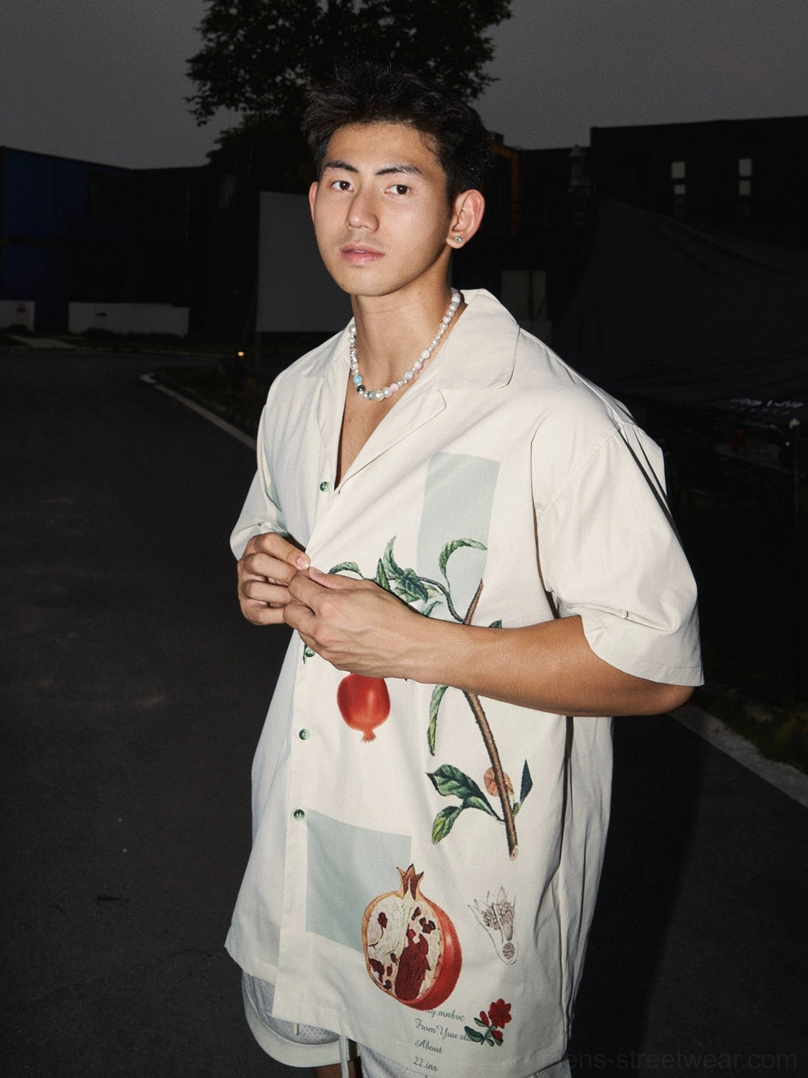 Three-quarter right view of a beige short sleeve camp shirt featuring detailed pomegranate branches and halved fruit motifs