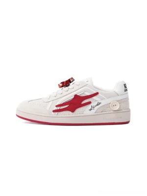 Beige and red retro training sneaker in a left front view with suede panels, red flame side motif, decorative floral shoelace charm, and red rubber outsole