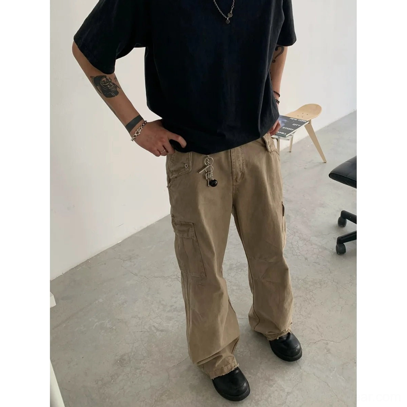 Front full-body view of beige relaxed straight leg cargo pants with side flap pockets and small hanging tag styled with a black tee and leather shoes