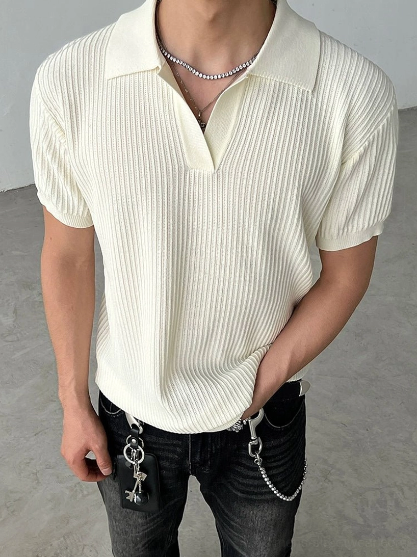 Full-body view of a model wearing a cream beige ribbed knit polo shirt with open collar black jeans and chain wallet styling