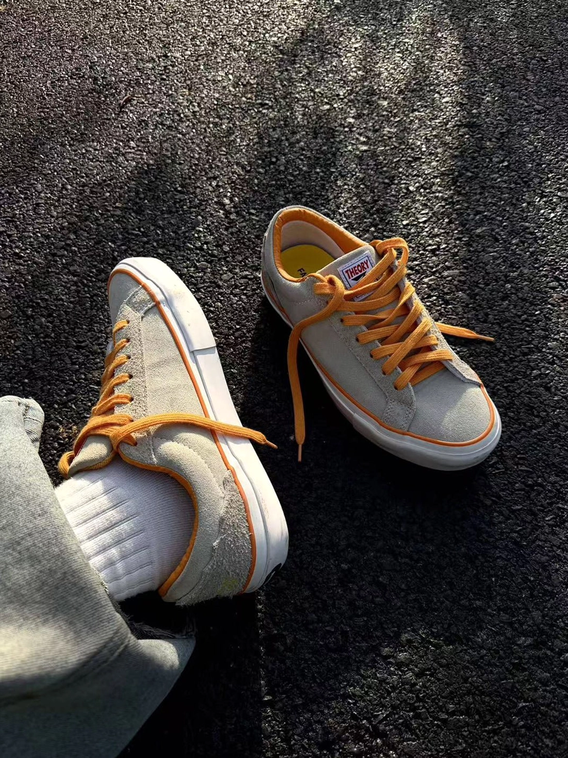 Side overhead view of beige suede skate shoe with orange inner lining, worn with white crew socks and denim pants