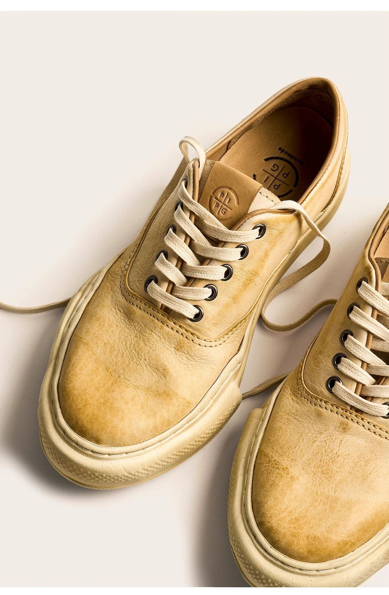 Top-down view of beige washed leather sneakers with loose laces, branded leather insoles, distressed uppers, and substantial aged retro soles