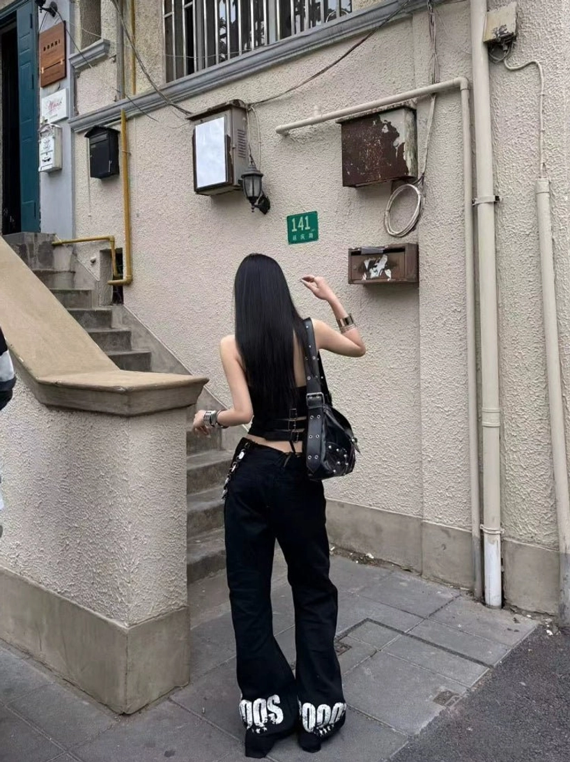 Rear view of black 2000s flare jeans with printed hems styled with a leather shoulder bag and Korean street fashion