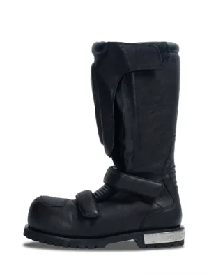 Black armored knee-high leather moto boot in left side profile with molded shin guard straps silver heel cap and rugged lug sole