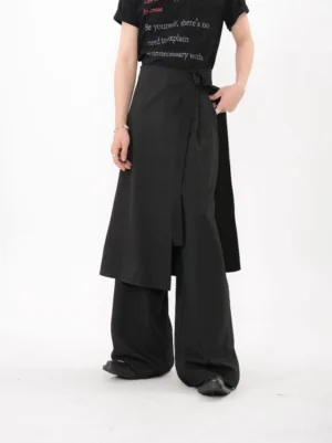 Black asymmetric wrap layer wide leg trousers in a left front three-quarter view with a draped apron overlay and graphic black T-shirt styling