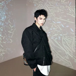 Side profile of black cropped asymmetric zip techwear jacket styled with a crossbody bag and layered streetwear hem