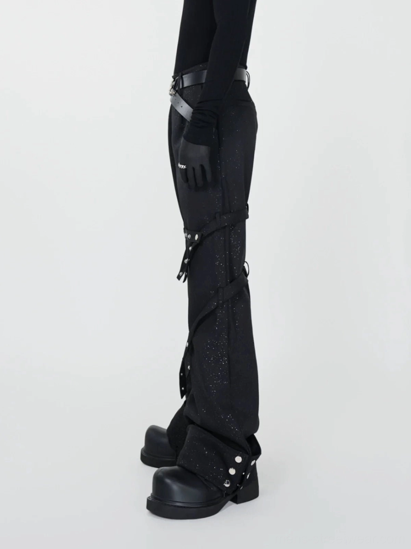 Side view of black avant-garde streetwear flare pants with spiral straps silver rivets glitter finish and industrial details