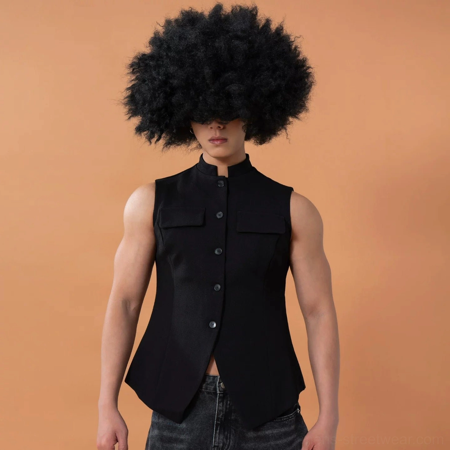Front three-quarter view of a black avant-garde tailored vest with curved asymmetrical pointed hem, button front, chest pockets, and sculpted shoulders