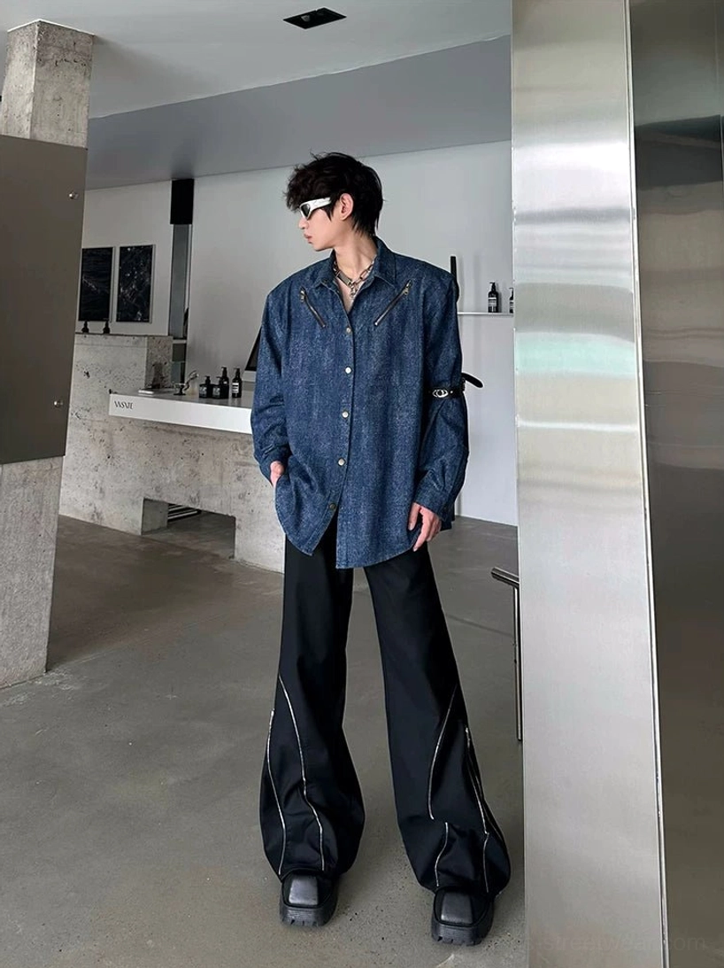 Black avant-garde streetwear wide-leg zip trousers shown from the side with relaxed oversized legs, silver zipper seam details, and a denim shirt outfit