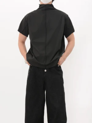 Rear full-body view of a black back seam mock neck short-sleeve shirt styled with black wide-leg jeans in a minimalist studio