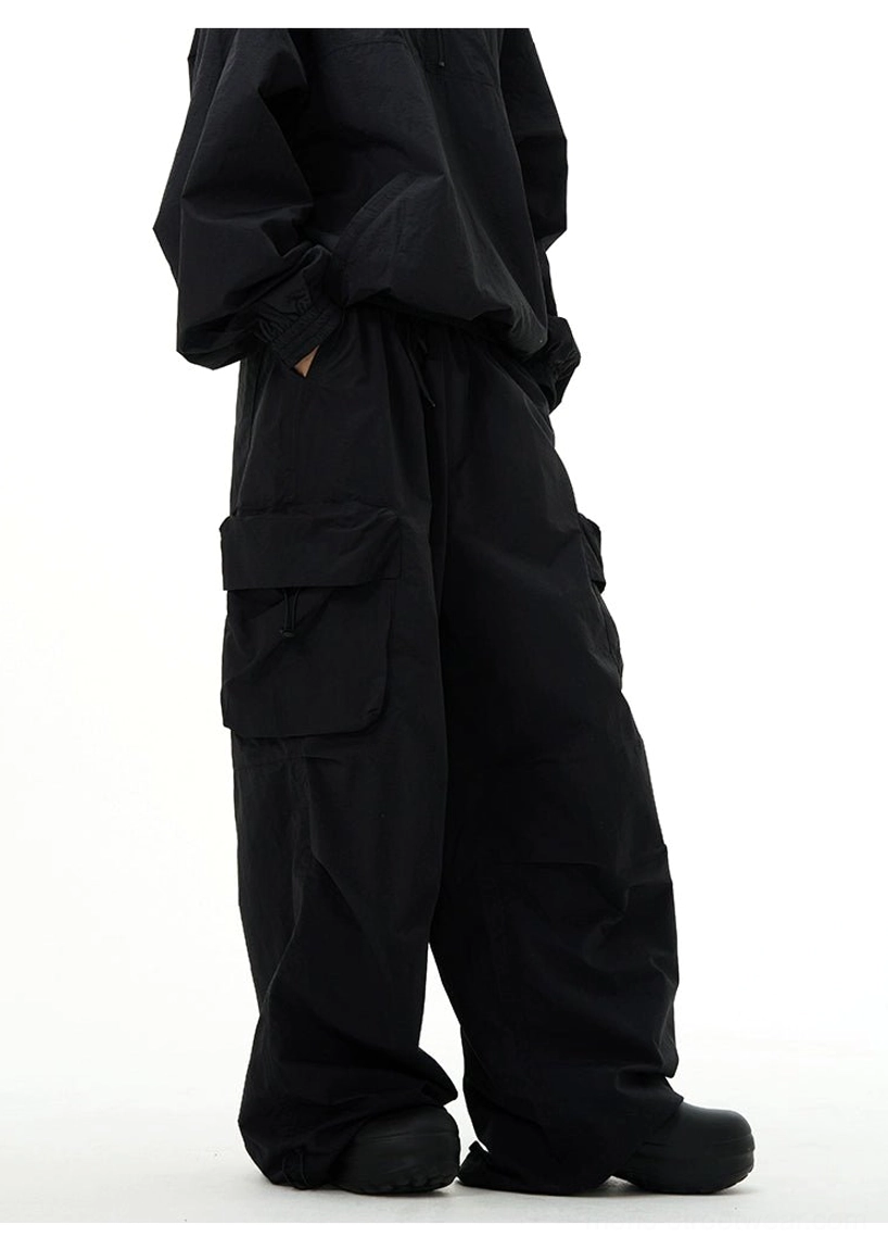 Three-quarter close-up of black baggy cargo pants showing large flap side pockets and wide-leg streetwear silhouette