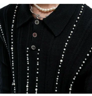 Close-up of black beaded knit polo sweater showing polished buttons, ribbed cotton texture, vertical pearl-like embellishments and polo collar