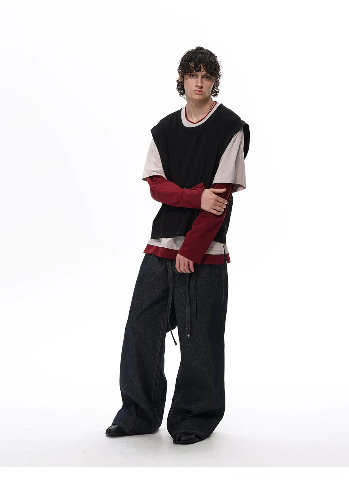 Side view of a male model wearing a black beige and burgundy faux layered vest tee top with wide-leg dark trousers