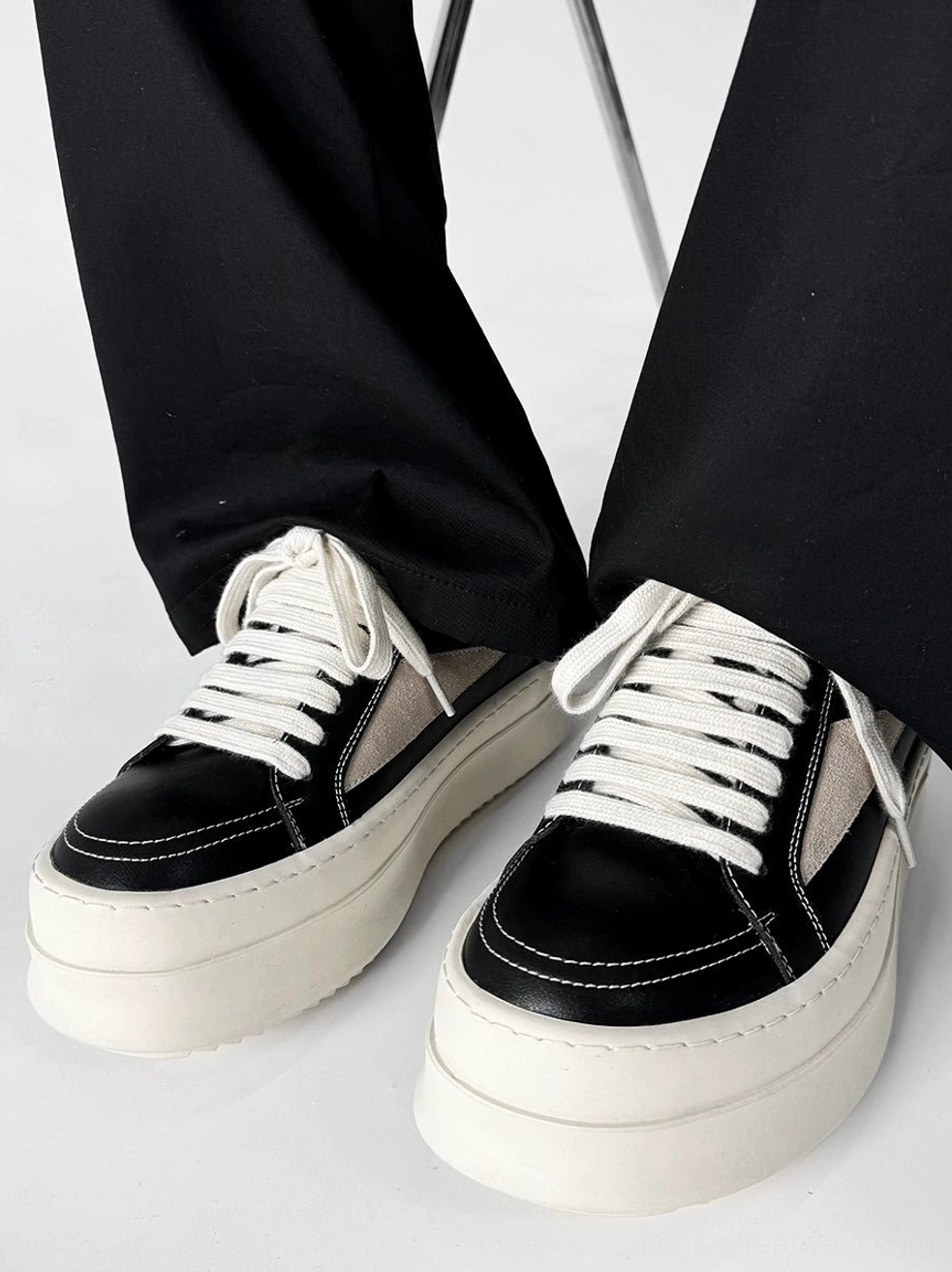 Black and beige chunky platform sneakers worn with wide-leg pants in a front view