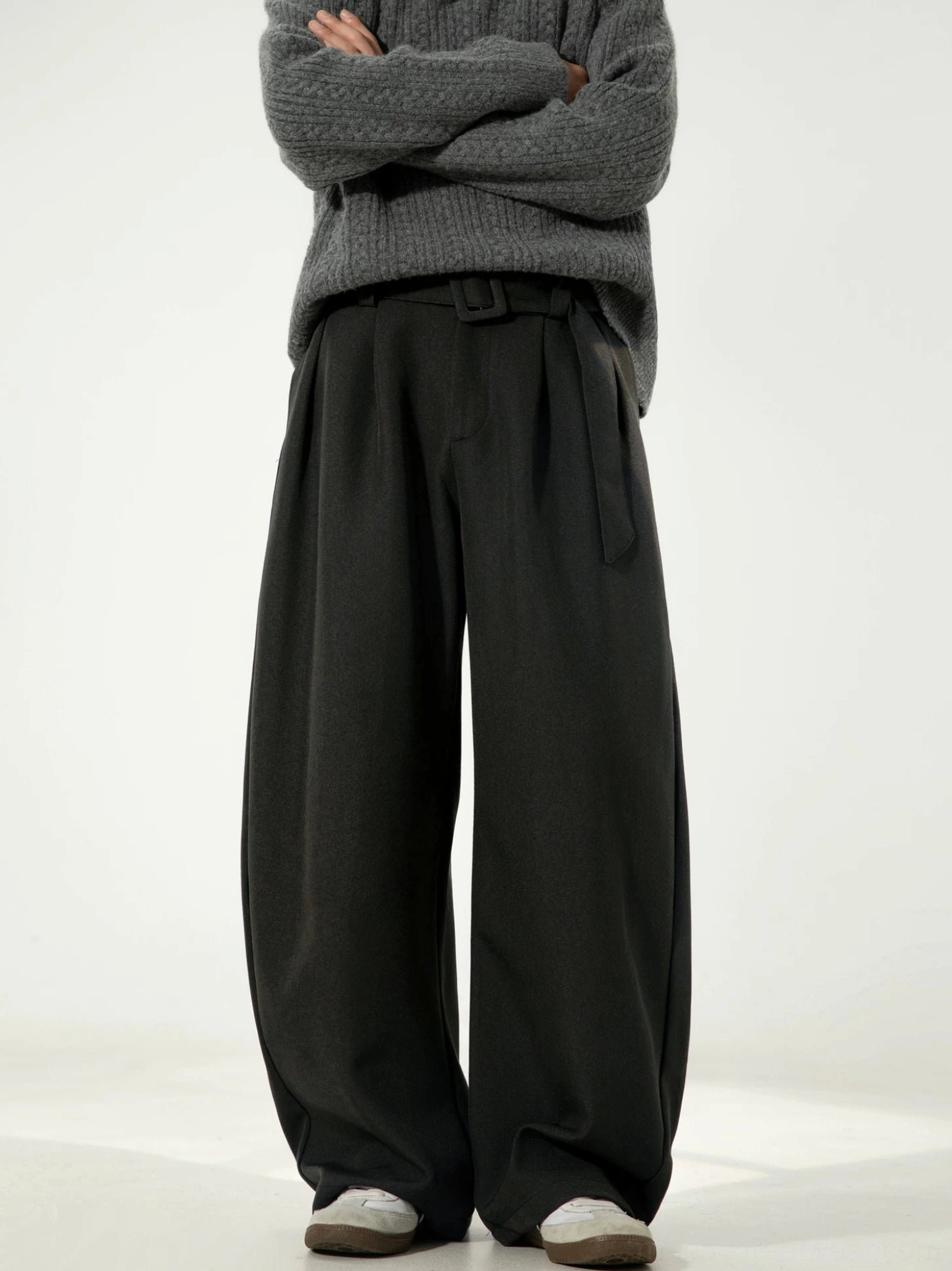 Male model wearing black belted wide-leg streetwear trousers with an oversized curved silhouette and mid-rise waist against a studio backdrop