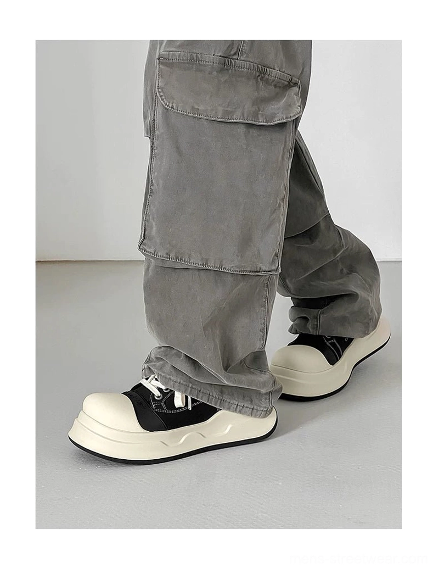 Side wearing view of black big-head platform sneakers with grey cargo pants, showing the rounded toe profile, stacked trouser hem, and thick platform sole