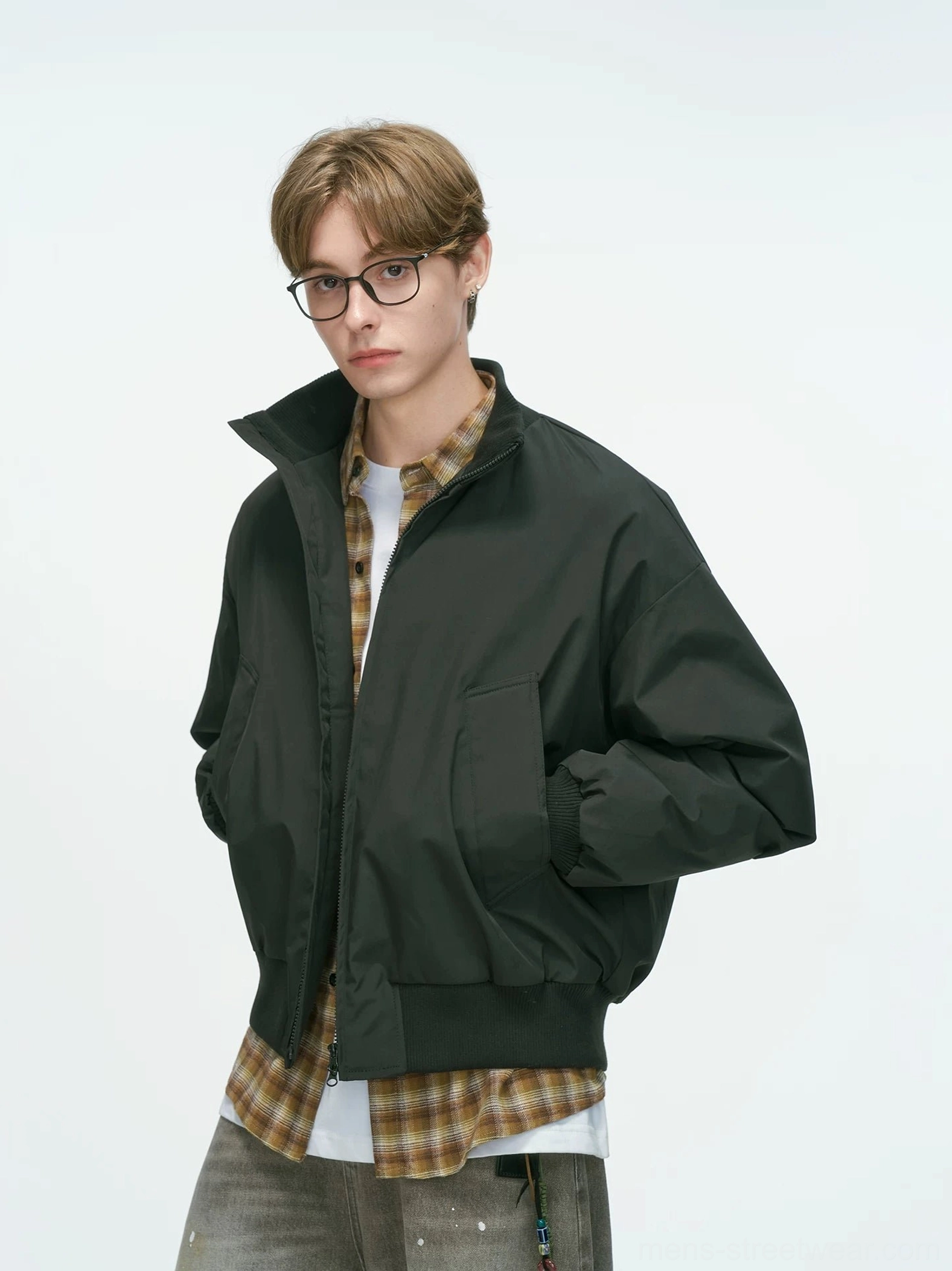 Black relaxed drop-shoulder bomber jacket with stand collar and ribbed cuffs, three-quarter front view on male model wearing layered casual streetwear