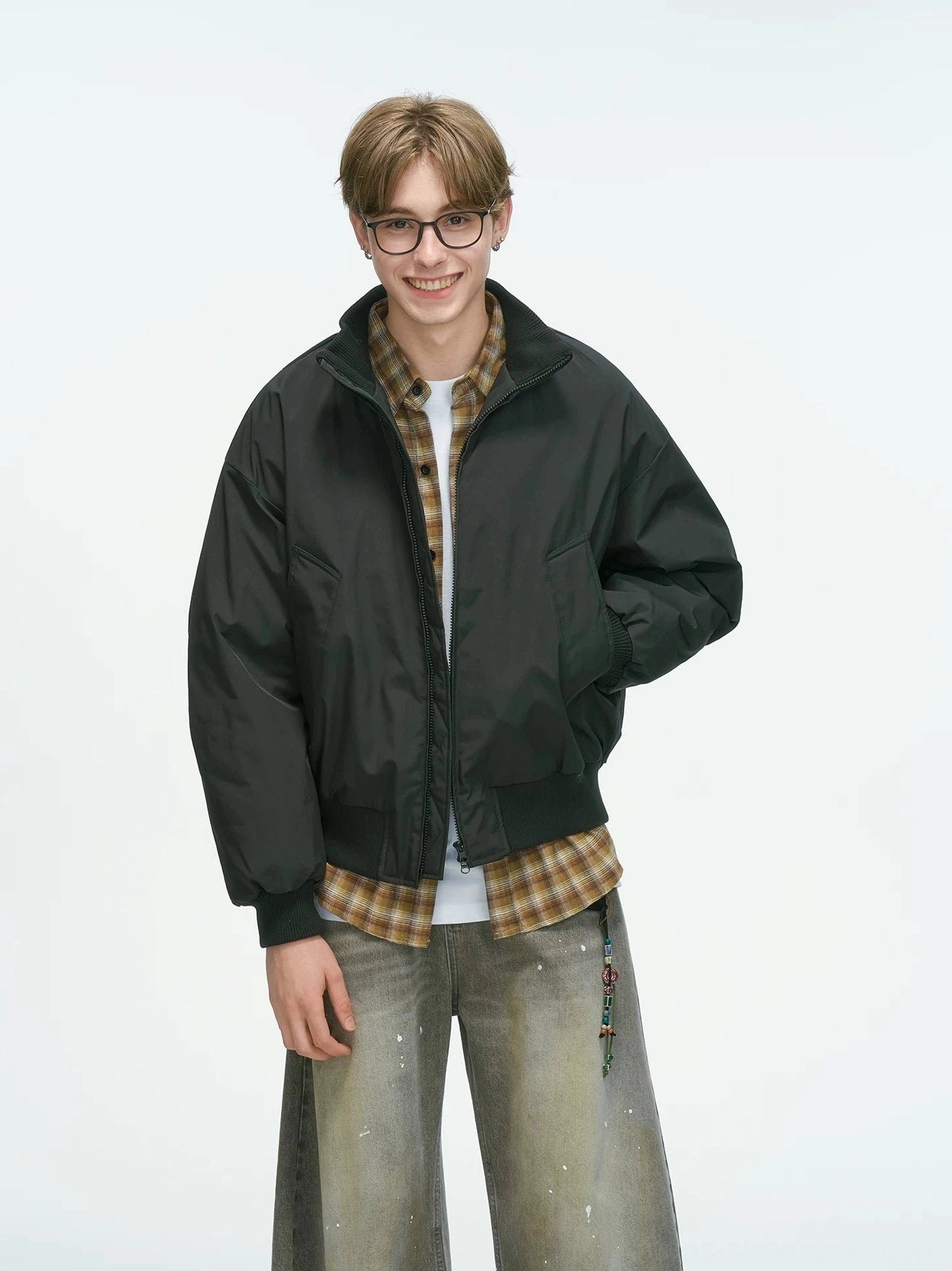 Black bomber jacket full front body shot with front patch pockets and drop shoulders, layered with plaid shirt and dirty-wash jeans streetwear aesthetic