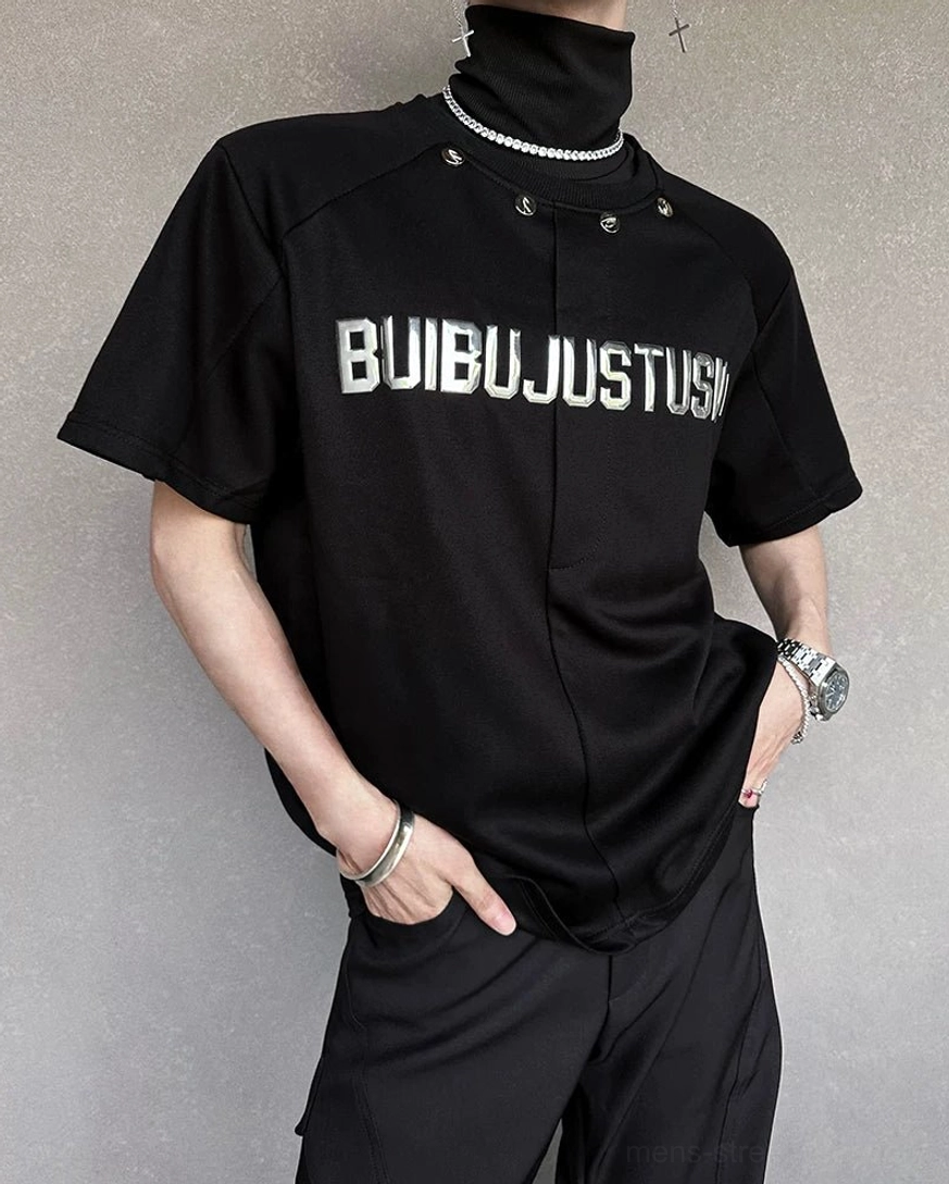 Left three-quarter view of a black boxy graphic T-shirt with metallic chest lettering, studded collar, and curved hem