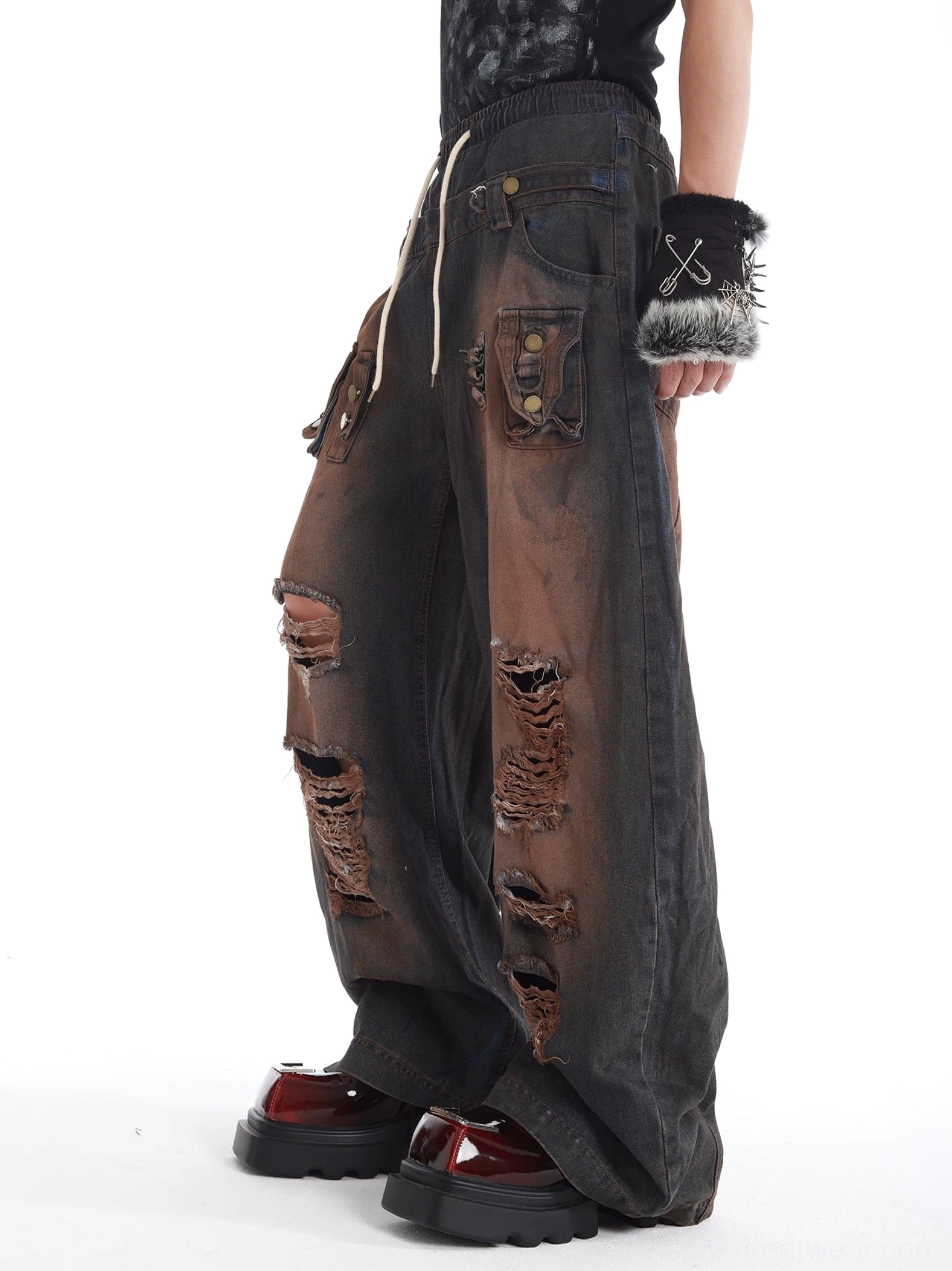 Side view of black and brown faded distressed cargo jeans with wide legs ripped cutouts and utility side pockets