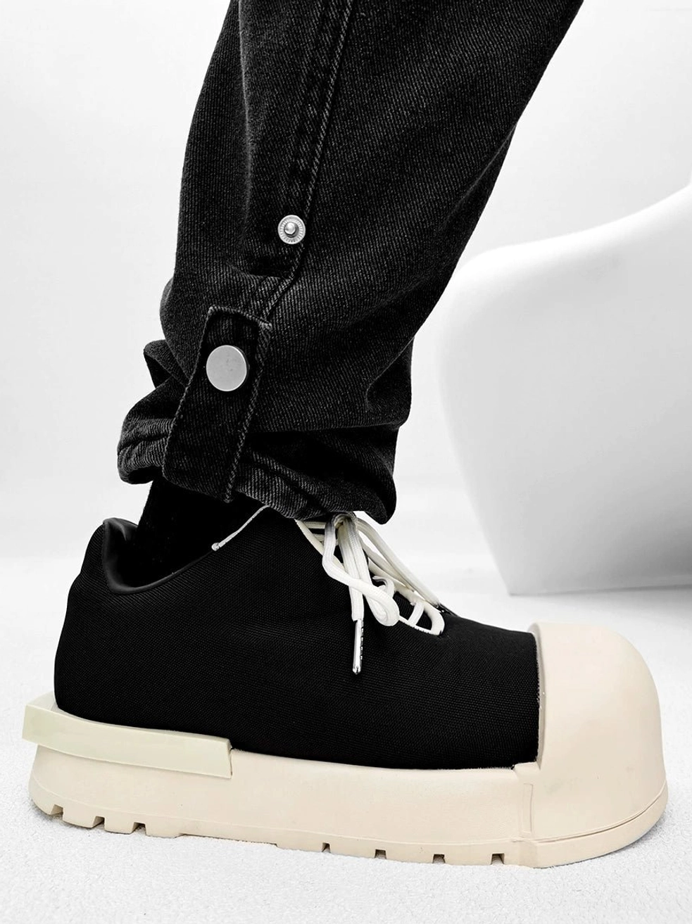 Minimalist black canvas platform sneakers with cream round toe, flat thick sole, white shoelaces, and rolled black denim styling