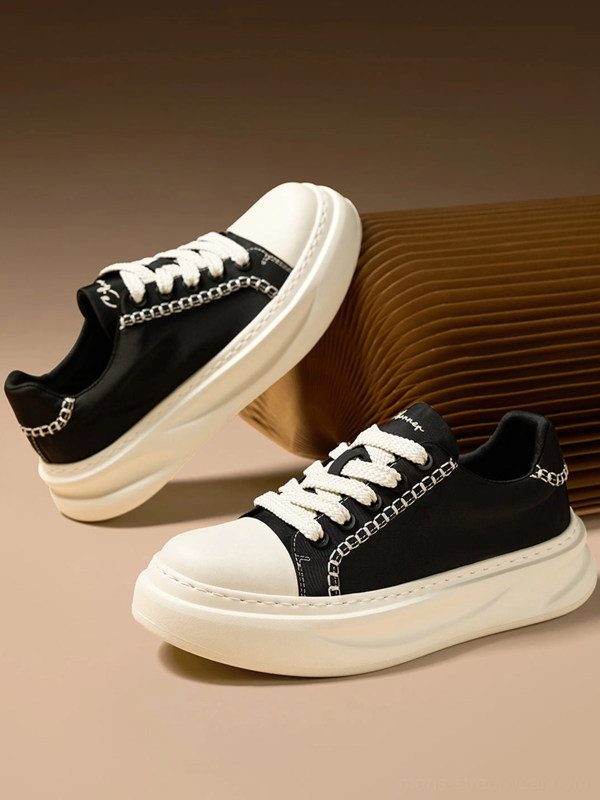 Black canvas platform sneakers photographed from a front-side angle showing the white toe cap, decorative stitching, chain trim, and chunky sole