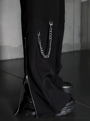 Close-up of black techwear cargo pants showing metal chain detail, matte fabric, and side zipper hem