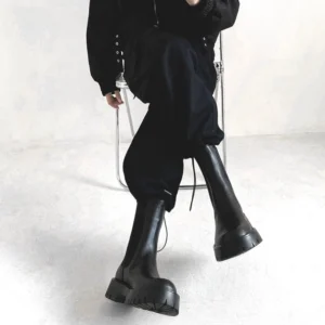 Black chunky Chelsea boots with glossy PU leather, elastic side panels, and a serrated platform sole styled with an all-black streetwear outfit
