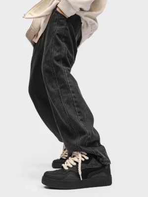 Black low-top platform street sneakers with cream rope laces worn with dark denim in a casual streetwear outfit