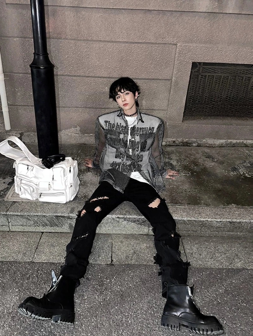 Streetwear model seated on urban stairs wearing black chunky square-toe platform boots with ripped black pants and a graphic long-sleeve top