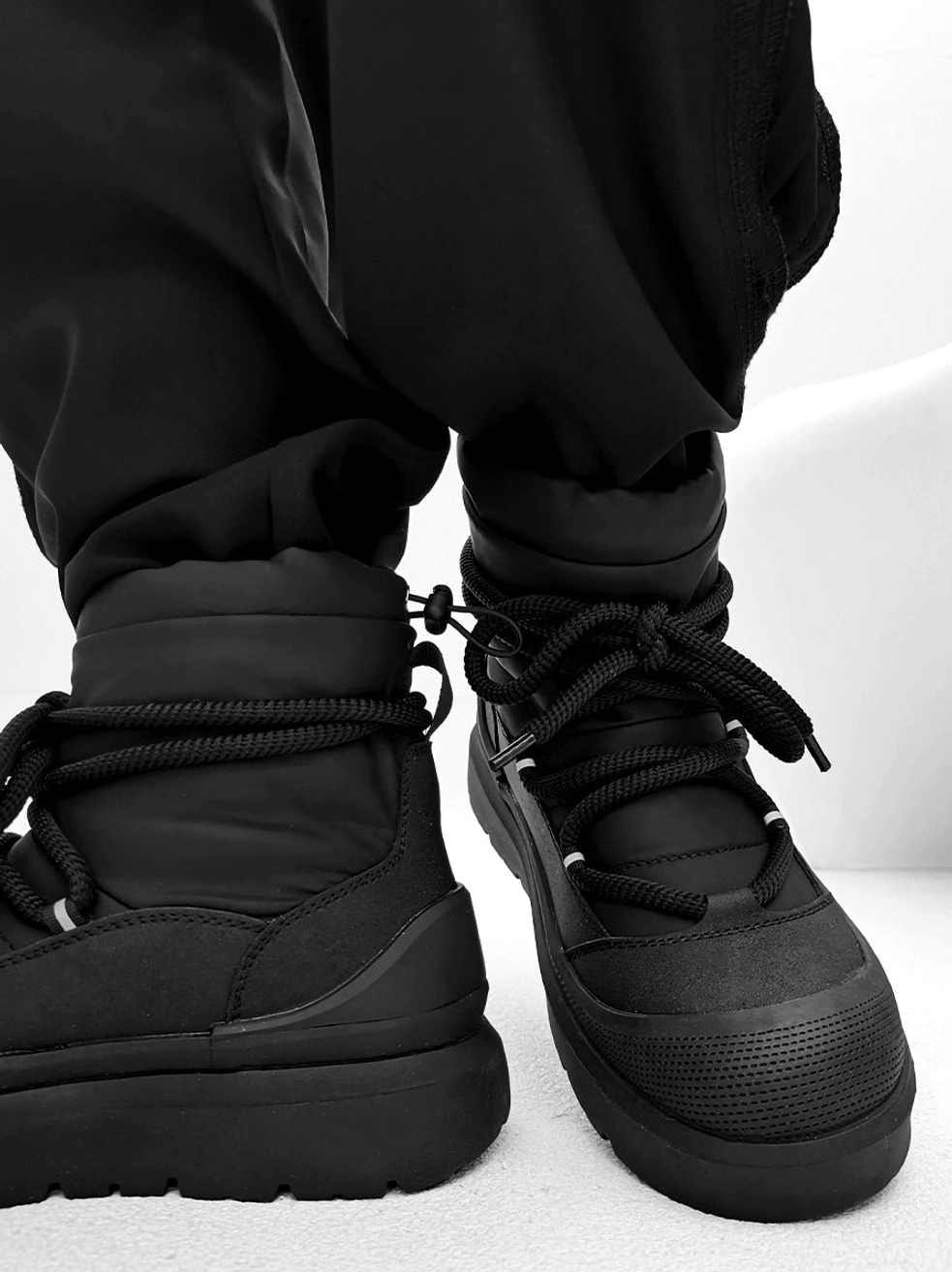 Rear side view of black chunky platform winter boots showing adjustable drawstring ankle collar and matte black finish