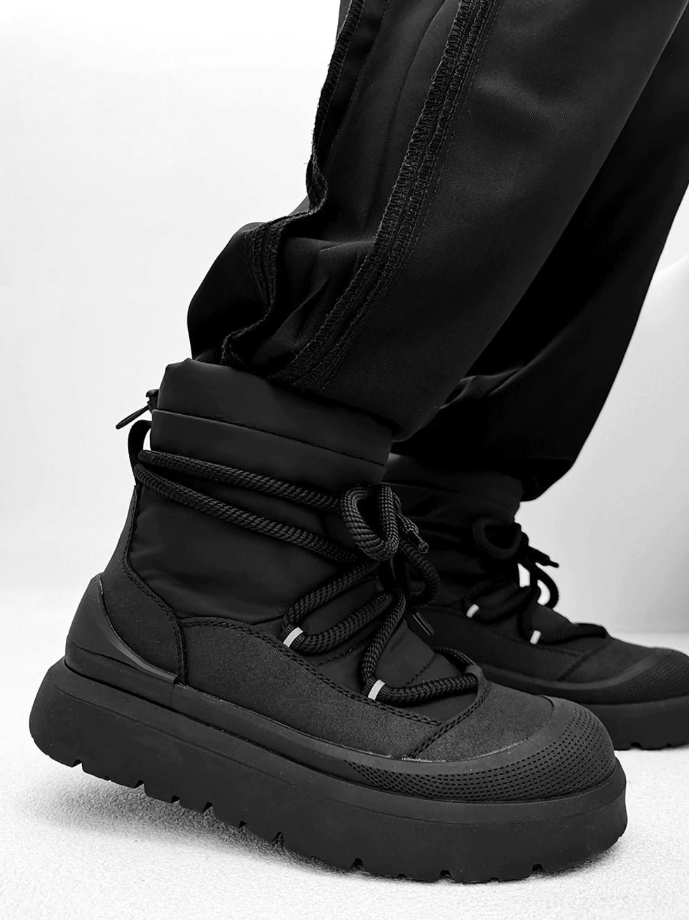 Side profile of black lace-up platform winter boots with mixed synthetic upper metal eyelets and chunky sole
