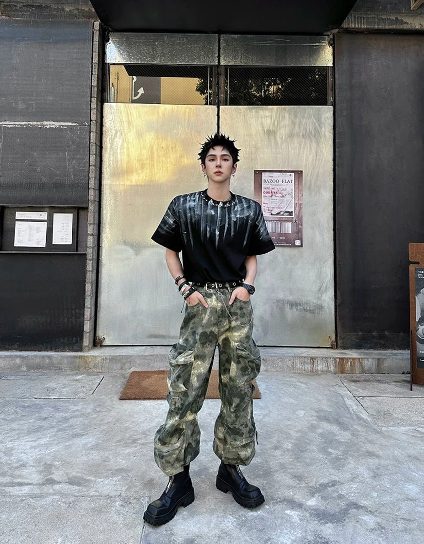 Streetwear model styling black chunky square-toe platform boots with a tie-dye tee, camouflage cargo pants, and leather wristbands