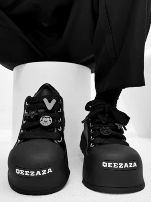 Black chunky square toe platform sneakers with decorative lace charms worn with black trousers in a top-down streetwear close-up