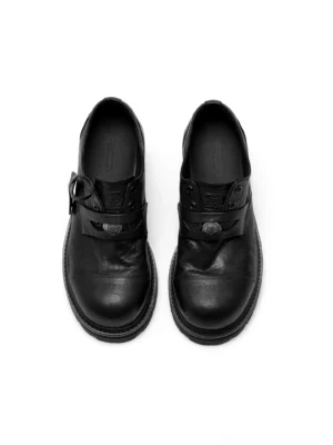 Black chunky sole strap derby shoes shown from a top-down front angle with washed leather upper, rounded cap toe, lace-up construction, decorative metal buckle, and industrial streetwear design