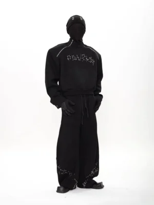 Black oversized constellation tech fleece streetwear set shown from a front three-quarter view with masked model, reflective raglan shoulder details, chest embroidery, and wide-leg pants