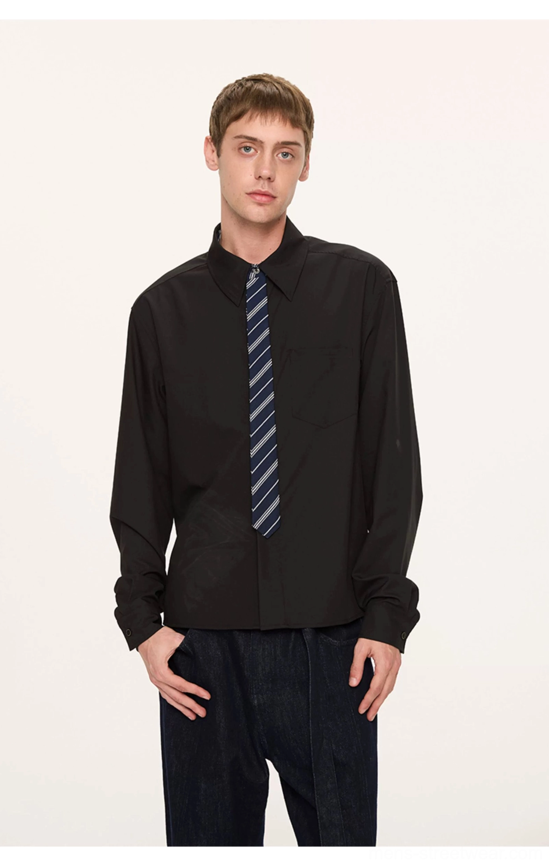 Male model wearing a black solid contrast collar shirt with blue striped tie and dark wide-leg trousers