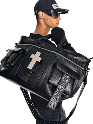 Male streetwear model carrying black cracked leather duffle tote bag with silver cross hardware and grommet detailed shoulder strap